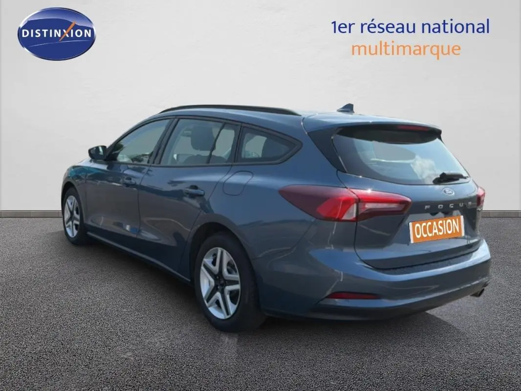 Vue 3/4 arrière droite d'une Ford Focus SW bleu foncé avec barres de toit et jantes classiques 16 pouces.