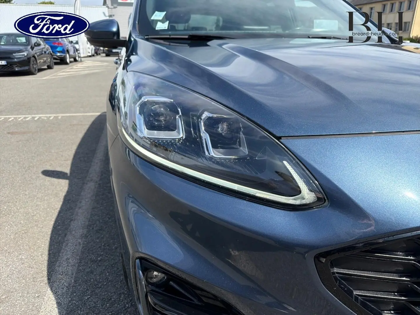 Gros plan sur l'avant droit bleu métallisé du Ford Kuga 2020, mettant en valeur le phare LED et la calandre noire.