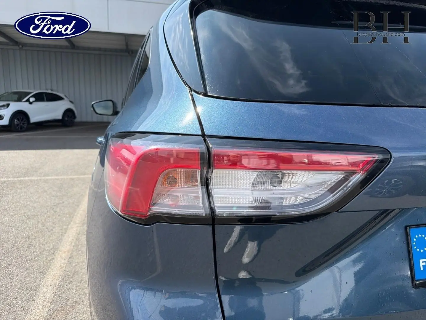 Gros plan sur le feu arrière gauche d’un Ford Kuga bleu Abysse 2020, avec reflet du ciel sur la carrosserie.