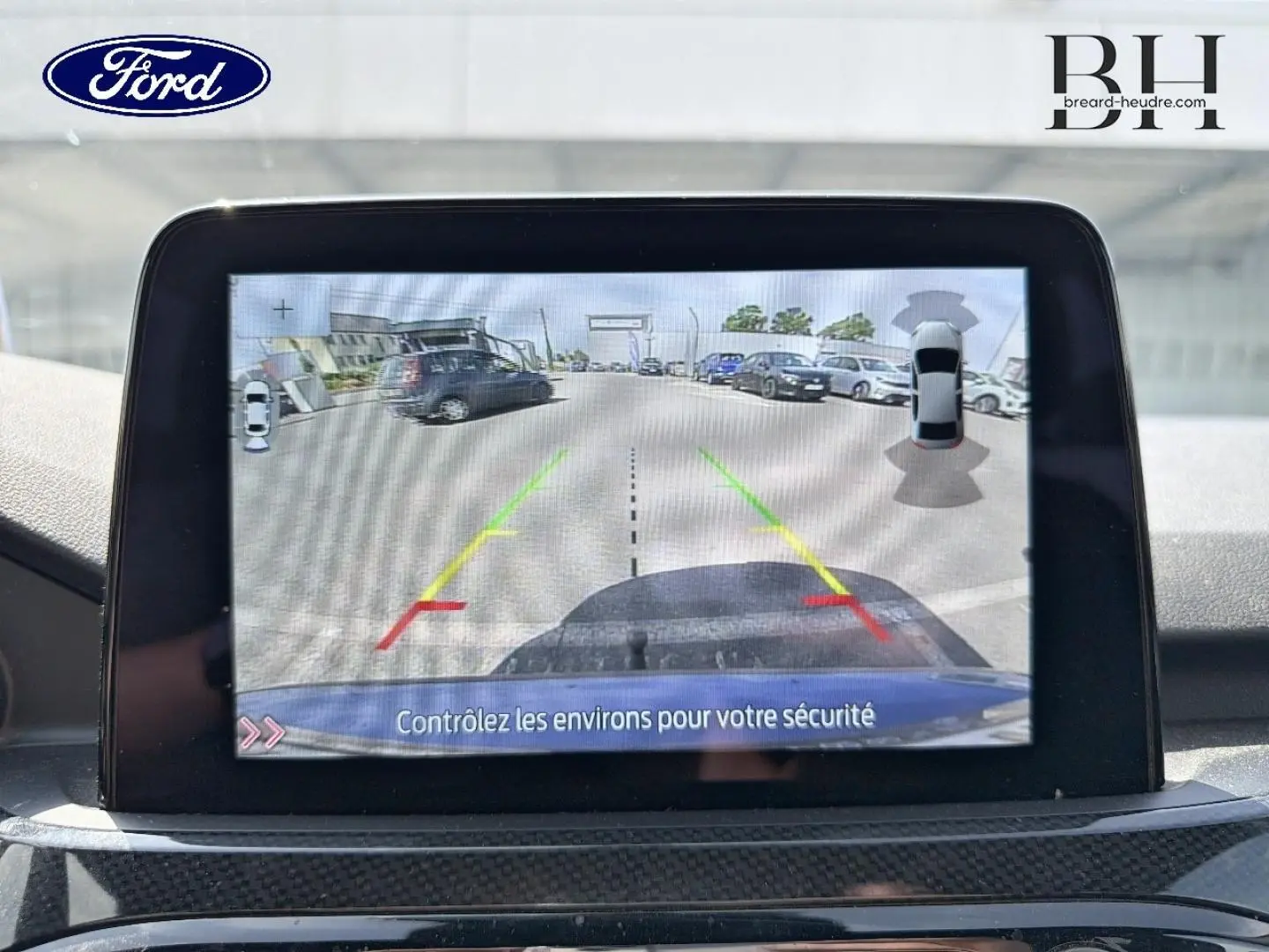 Écran tactile intérieur montrant la caméra de recul avec vue arrière et lignes de guidage du Ford Kuga bleu.