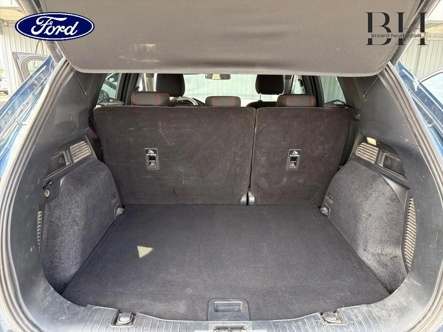 Coffre ouvert du Ford Kuga bleu, vue arrière montrant la banquette arrière noire et l'espace de chargement.