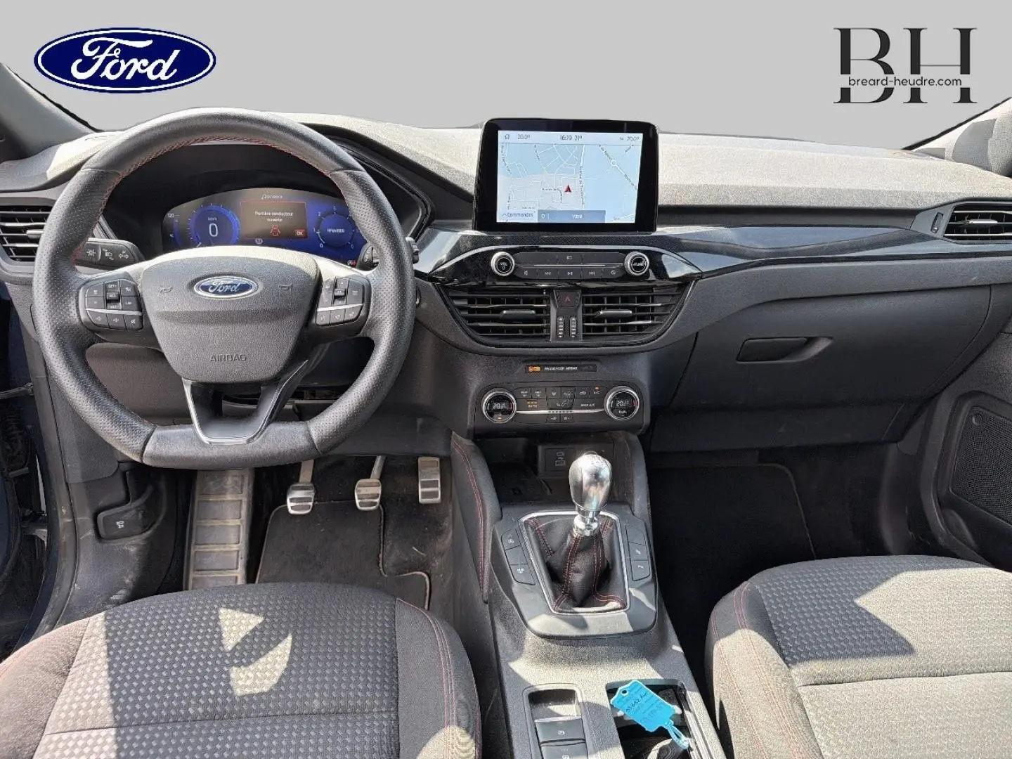 Vue intérieure avant du Ford Kuga bleu avec tableau de bord noir, volant cuir multifonction et levier de vitesse manuel.