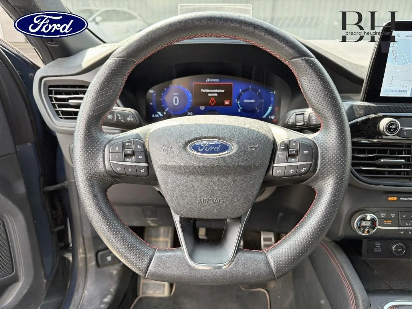 Vue rapprochée du volant cuir sport noir avec surpiqûres rouges du Ford Kuga 2020, tableau de bord digital en arrière-plan.