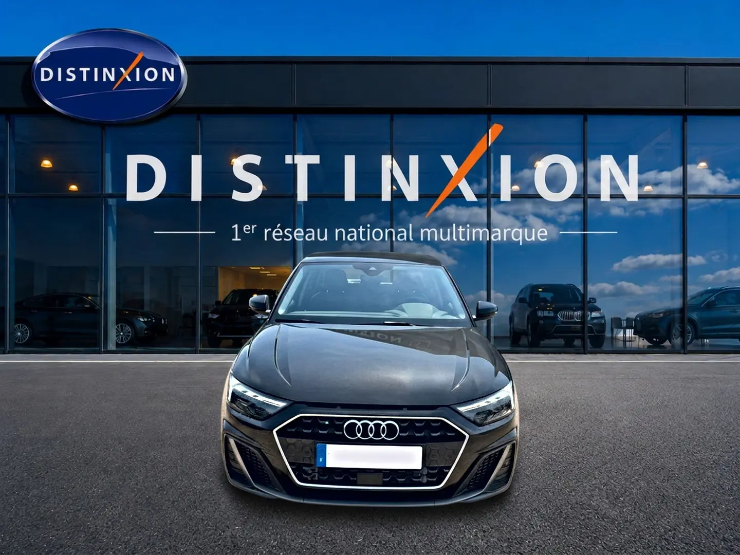 Vue de face d'une Audi A1 Sportback noire 2026 avec calandre hexagonale et phares LED, devant un showroom Distinxion.