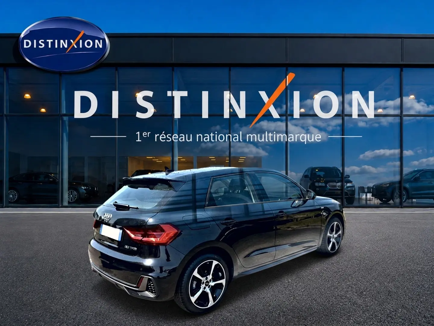 Audi A1 Sportback noir vue 3/4 arrière droit, avec jantes alu et becquet arrière, devant un showroom Distinxion.