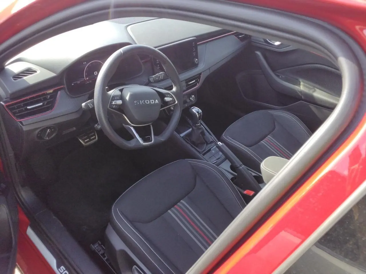 Vue intérieure côté conducteur de la Skoda Scala Monte-Carlo rouge Velvet, volant cuir et sièges noirs à bandes rouges.