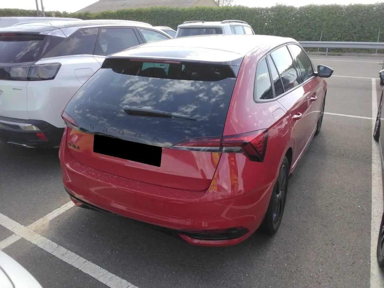 Vue 3/4 arrière droite d’une Skoda Scala rouge Velvet avec toit panoramique et hayon électrique sur parking.