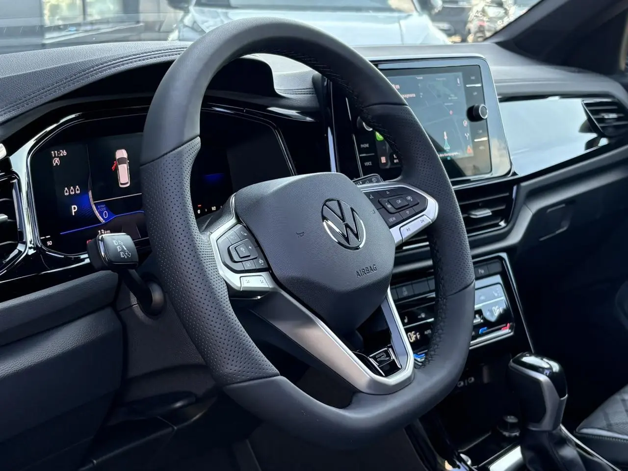 Vue intérieure centrée sur le volant sport multifonction noir du Volkswagen T-Roc 2025 avec tableau de bord digital et écran tactile.
