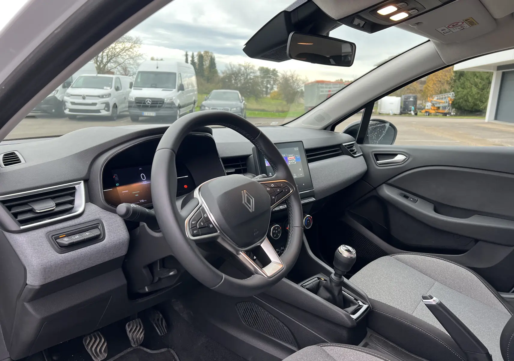 Intérieur de la Renault Clio V 2025 montrant le volant cuir, tableau de bord numérique et levier de vitesse manuel côté gauche.
