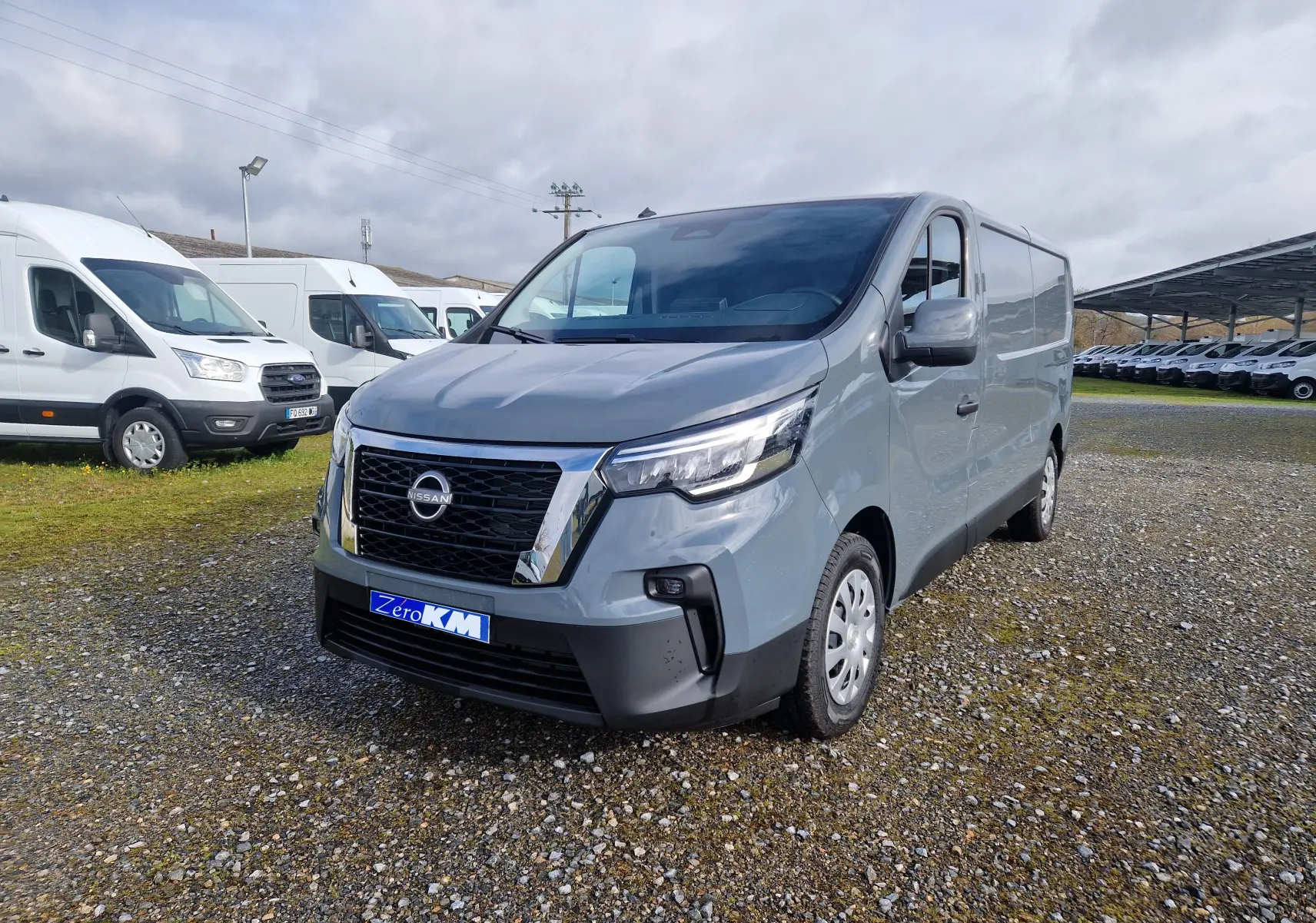 Nissan Primastar gris urbain vu en 3/4 avant droit sur un parking de véhicules utilitaires.