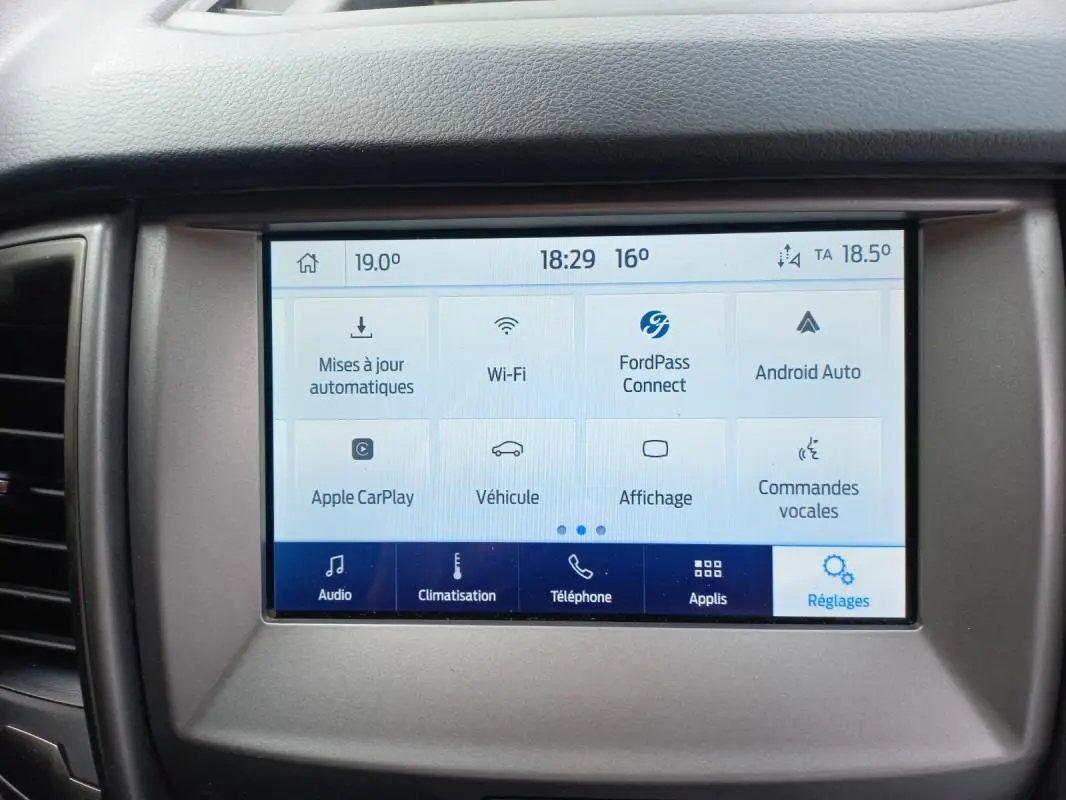 Tablette tactile centrale du Ford Ranger blanc 2022, affichant le menu des réglages avec options connectivité et climatisation.