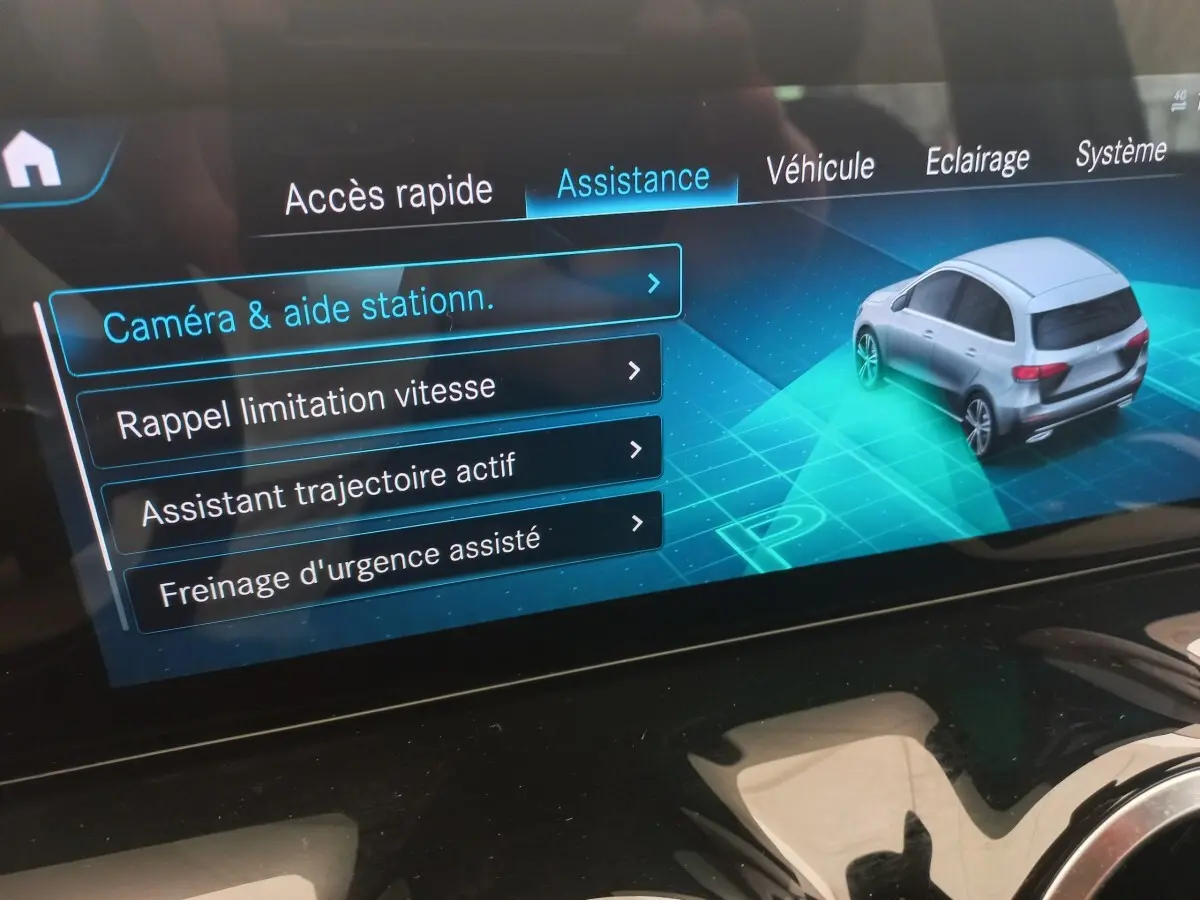 Écran tactile intérieur affichant le menu assistance avec une voiture grise vue en 3/4 arrière.