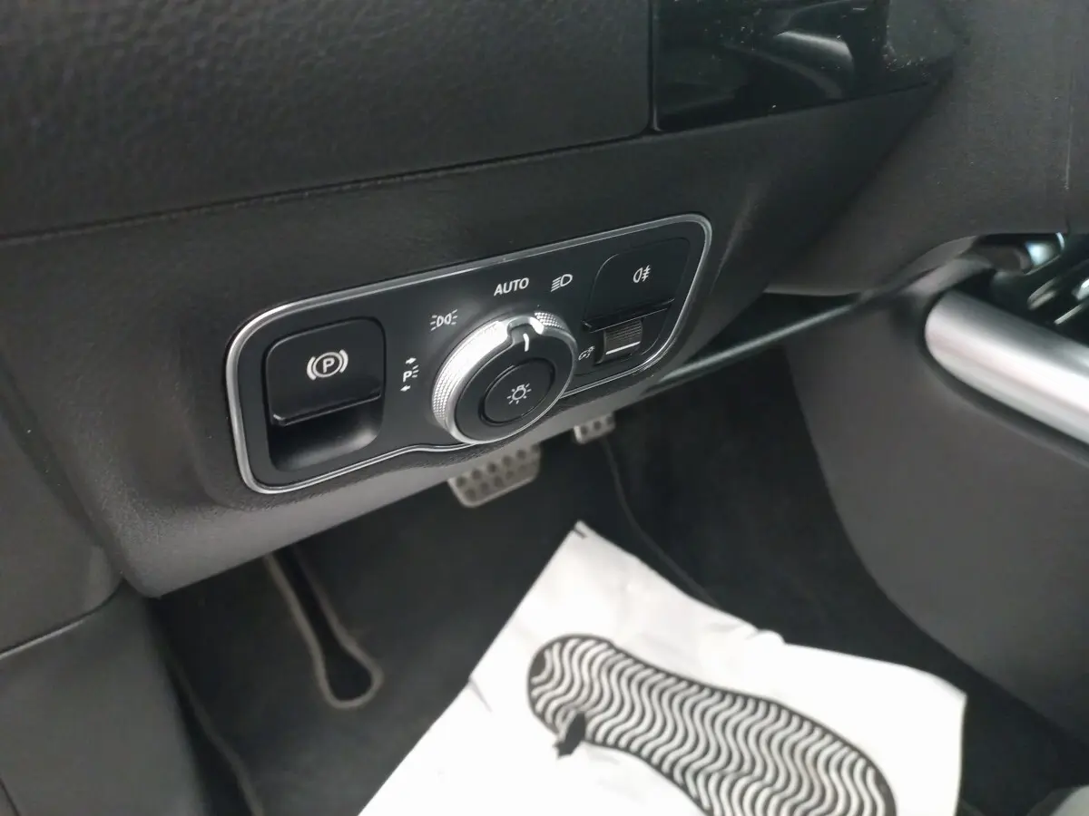 Détail du panneau de commande des phares et frein à main électrique côté conducteur dans une Mercedes Classe A noire.