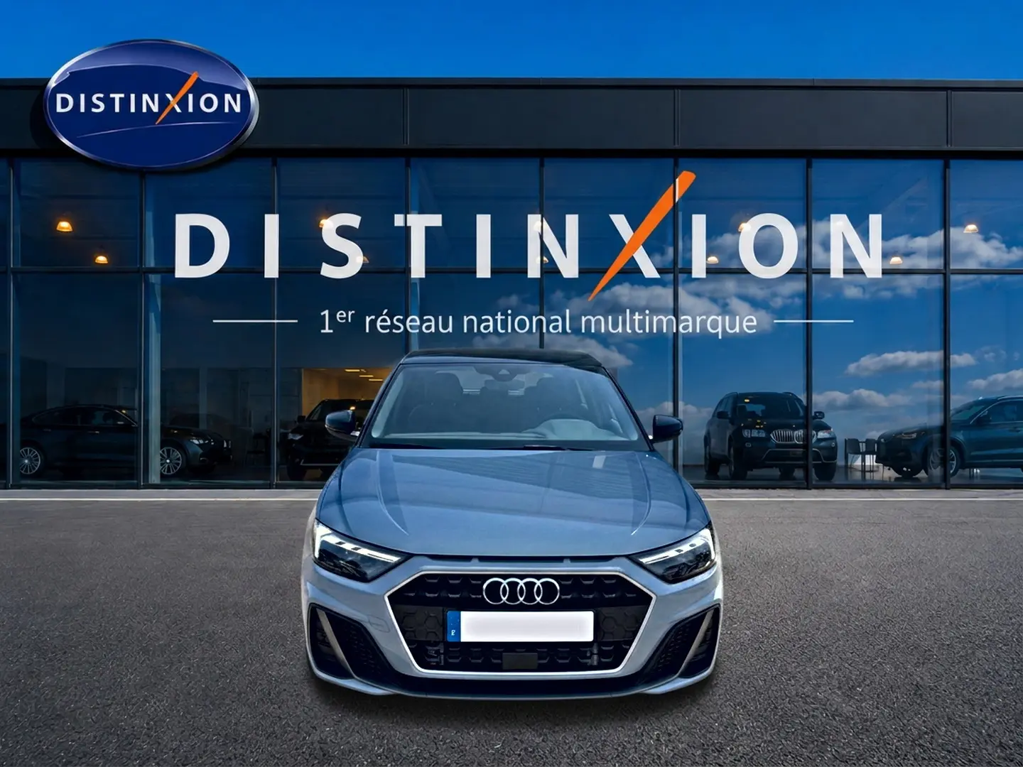 Vue avant d'une Audi A1 Sportback gris arrow avec calandre noire, stationnée devant une vitrine Distinxion.