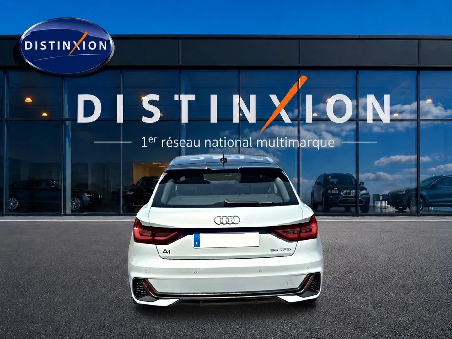 Vue arrière d'une Audi A1 Sportback 30 TFSI gris arrow avec feux LED et becquet arrière, devant une vitrine Distinxion.
