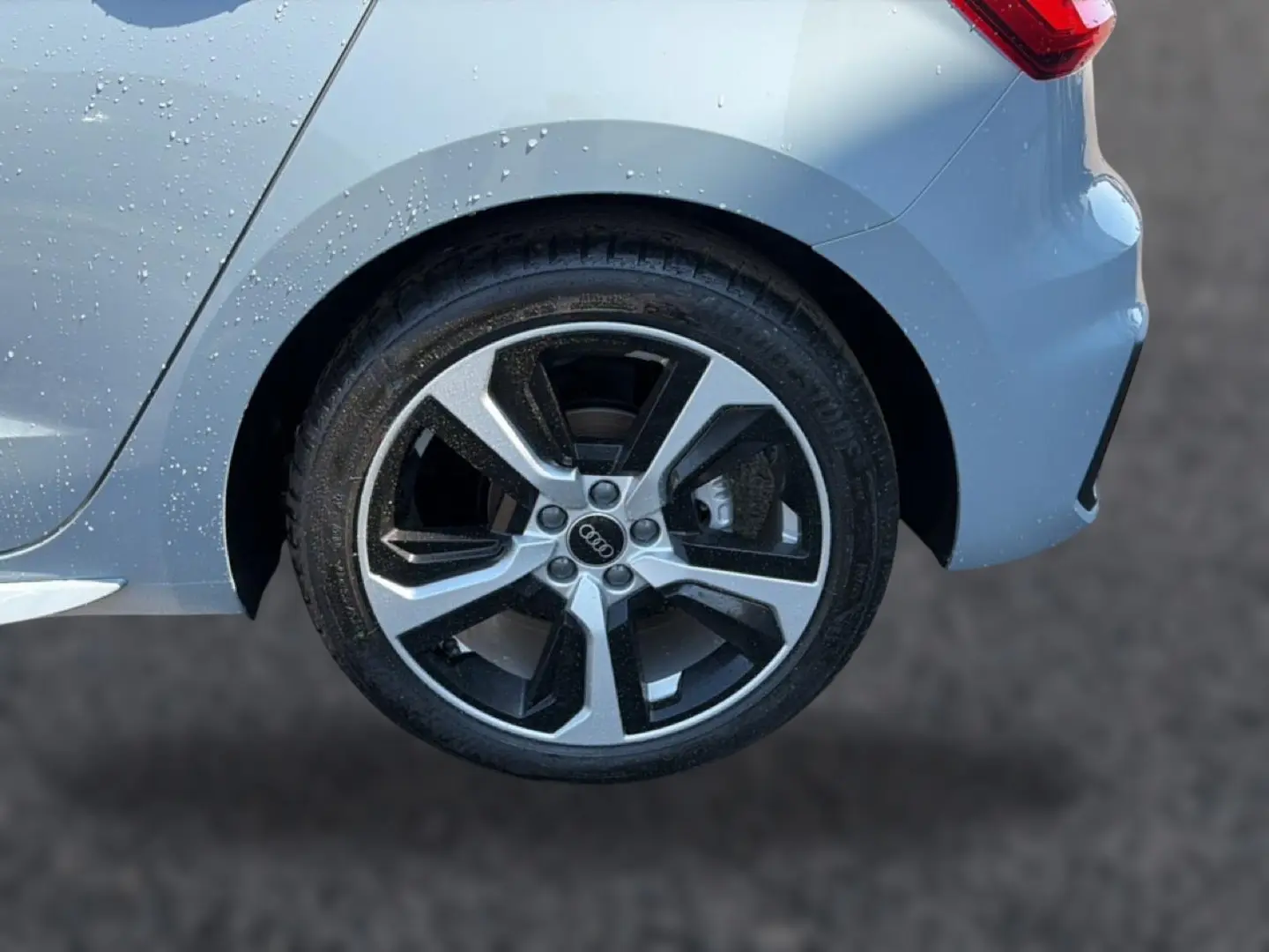 Gros plan sur la roue arrière droite de l'Audi A1 Sportback gris arrow avec jante alu bicolore et carrosserie mouillée.