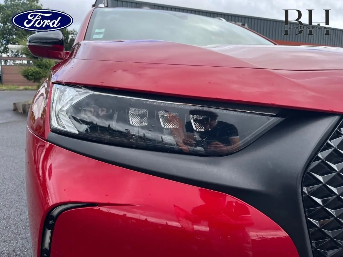Gros plan sur le phare avant gauche rouge Absolu du DS7 Crossback avec calandre noire et reflets sur la carrosserie.