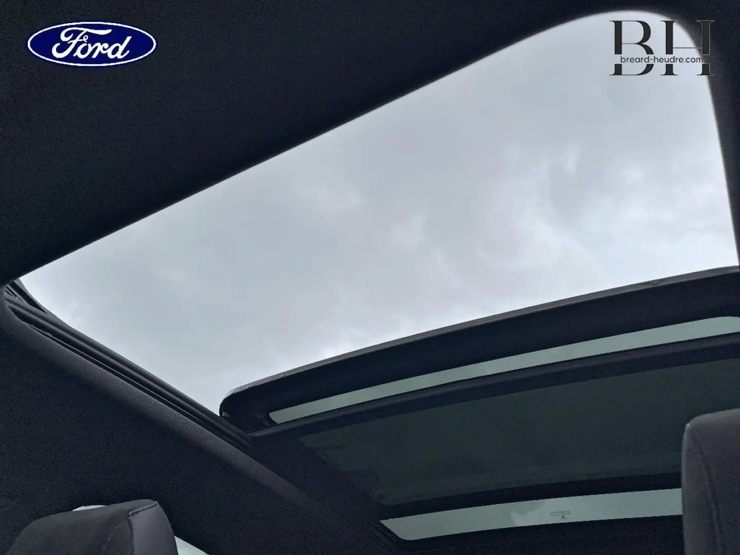 Vue intérieure du toit ouvrant panoramique ouvert du DS7 Crossback Rouge Absolu, montrant le ciel nuageux au-dessus.