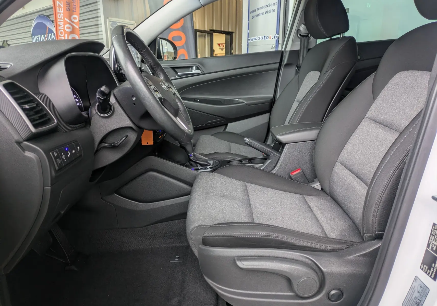 Vue intérieure côté conducteur du Hyundai Tucson 2020 blanc, sièges tissu gris et noir avec console centrale visible.