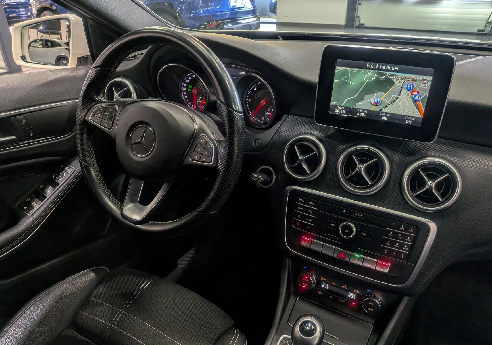 Vue intérieure côté conducteur de la Mercedes Classe A 200d 2016 avec tableau de bord noir et écran de navigation allumé.