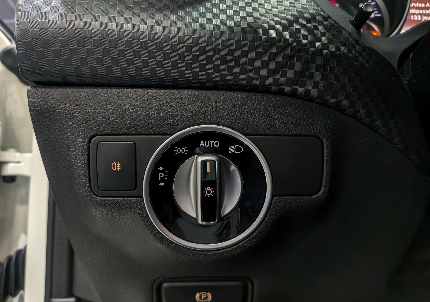 Gros plan sur le bouton de commande des phares et feux antibrouillard dans l'habitacle noir d'une Mercedes Classe A blanche.