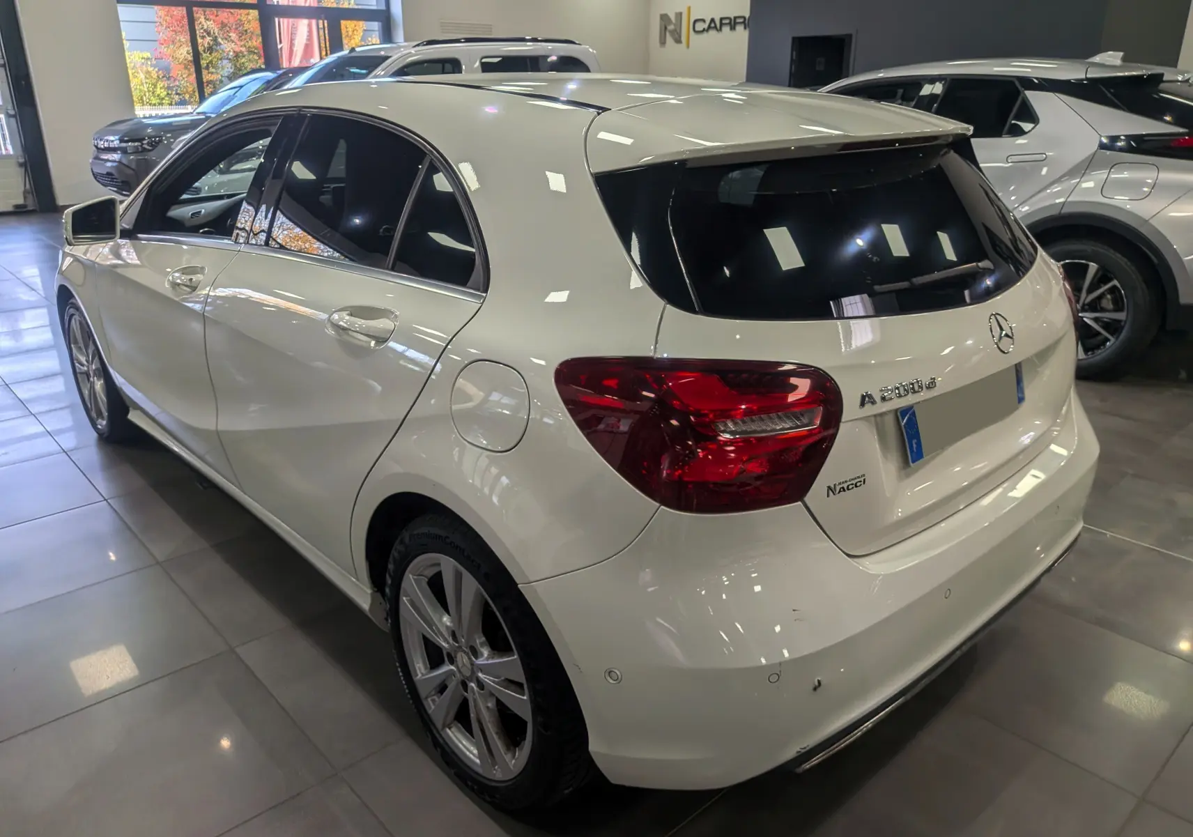 Vue 3/4 arrière droite d'une Mercedes Classe A 200d blanche en showroom, avec vitres teintées et jantes alliage.