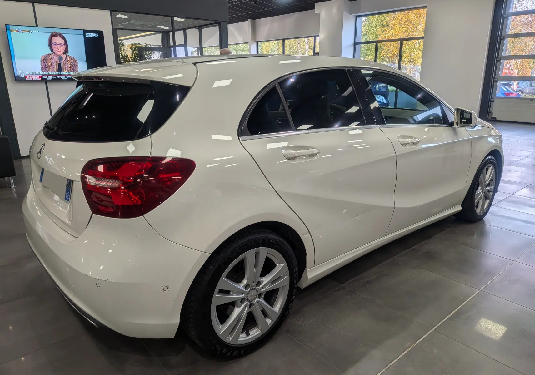 Vue 3/4 arrière droite d'une Mercedes Classe A 200d blanche 2016 en showroom avec vitres teintées et jantes alliage.