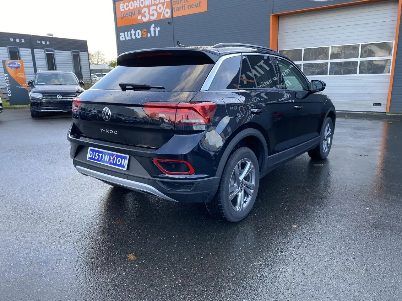Volkswagen T-Roc noir en 3/4 arrière droit, avec vitres surteintées et jantes alliage visibles sur parking humide.