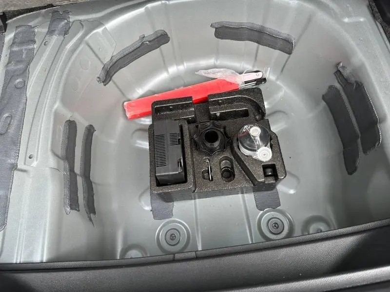 Coffre ouvert du SEAT Arona 2025, vue plongeante sur le rangement gris métallique avec kit de dépannage et triangle de signalisation rouge.