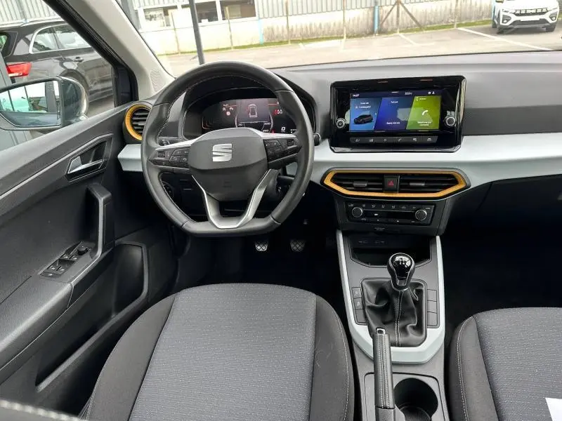 Vue intérieure avant du SEAT Arona 2025, tableau de bord noir avec touches orange autour des aérateurs et écran tactile central.