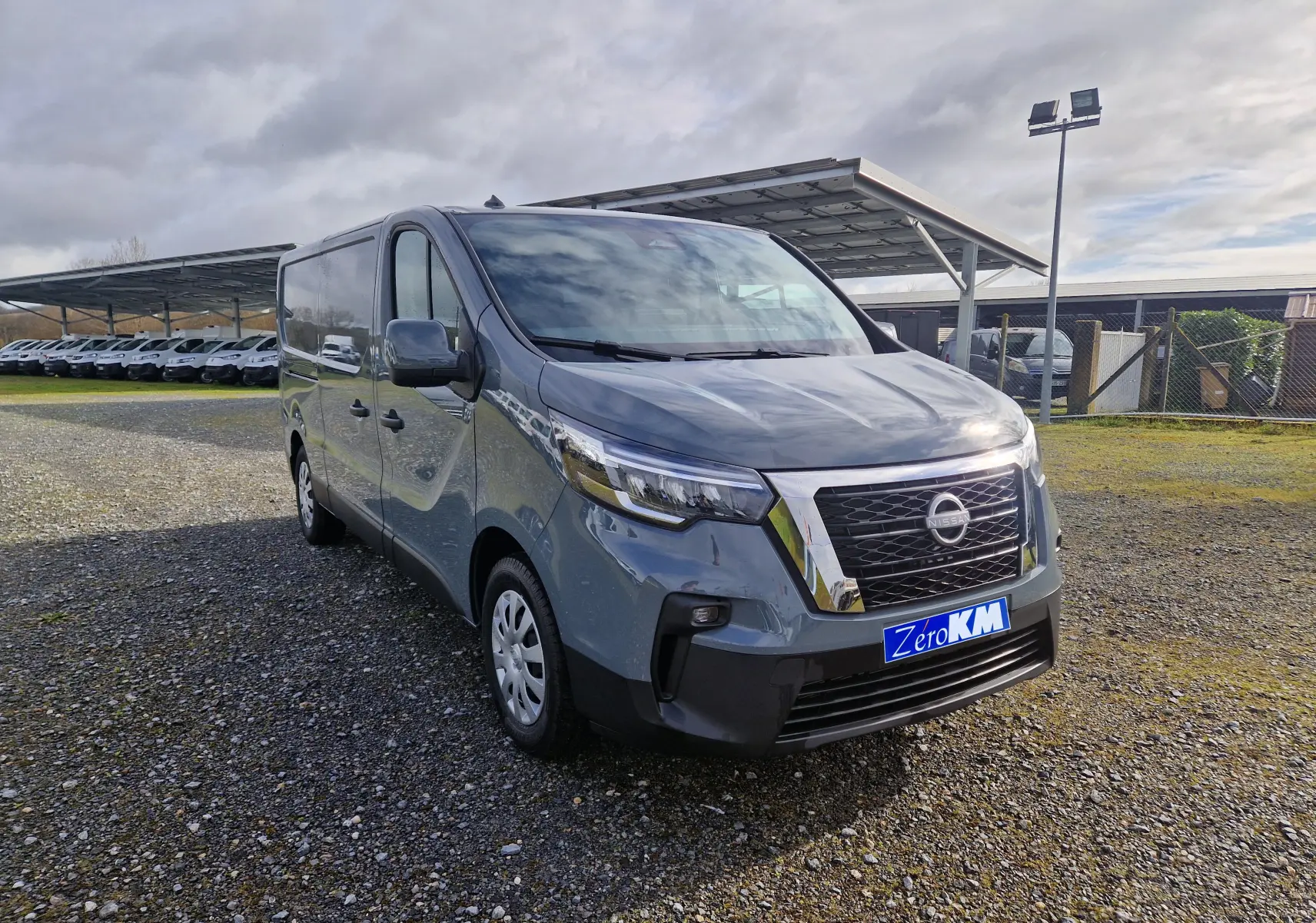 Nissan Primastar gris urbain en vue 3/4 avant droit, avec calandre chromée et plaque "Zero KM" visible.
