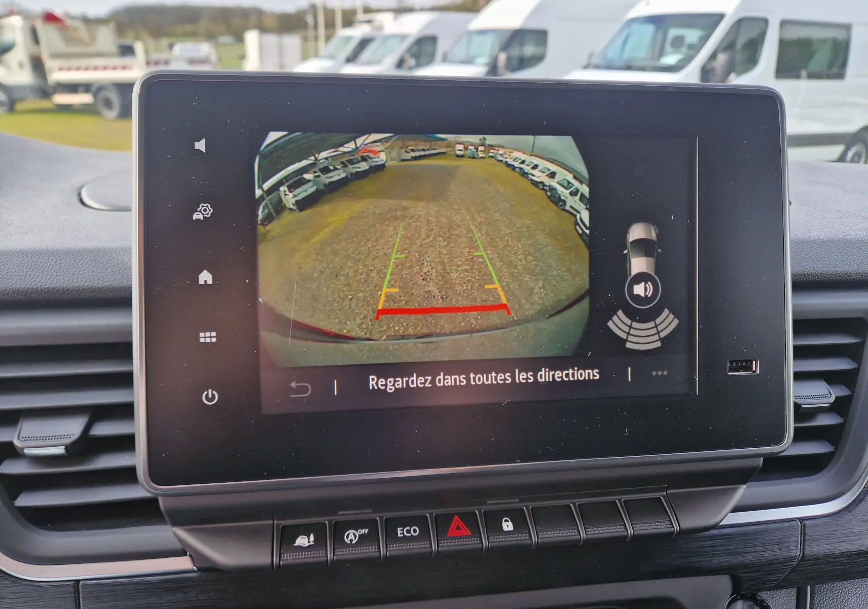 Écran central montrant la caméra de recul du Nissan Primastar gris urbain, avec lignes de guidage et alertes de proximité.