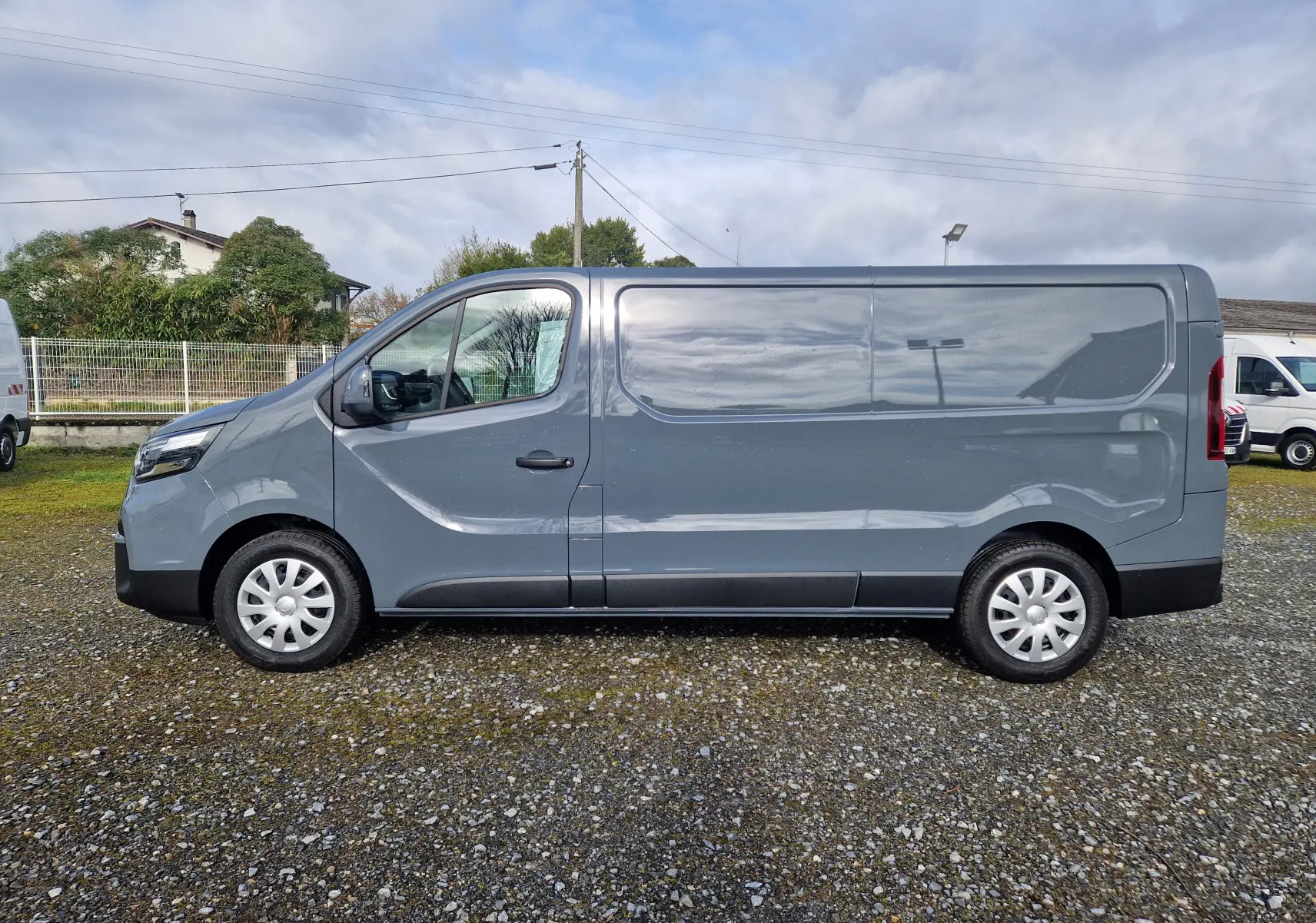 Vue de profil côté gauche d’un utilitaire Nissan Primastar gris urbain, version L2H1 avec porte latérale coulissante.