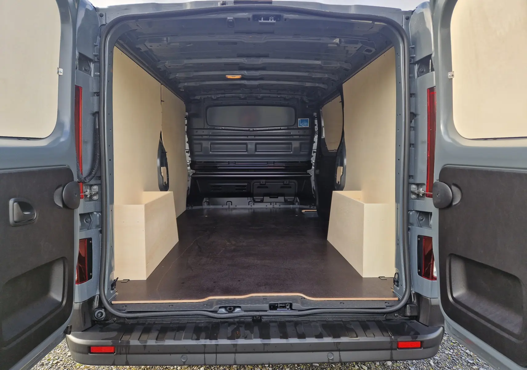 Vue arrière du Nissan Primastar gris urbain 2025, montrant l’intérieur du coffre avec aménagement bois Pack Cargo.