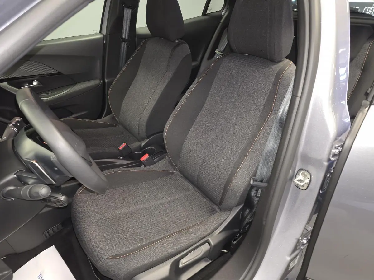 Vue intérieure côté conducteur du Peugeot 2008 gris 2025, sièges tissu gris avec surpiqûres orange et volant compact cuir.