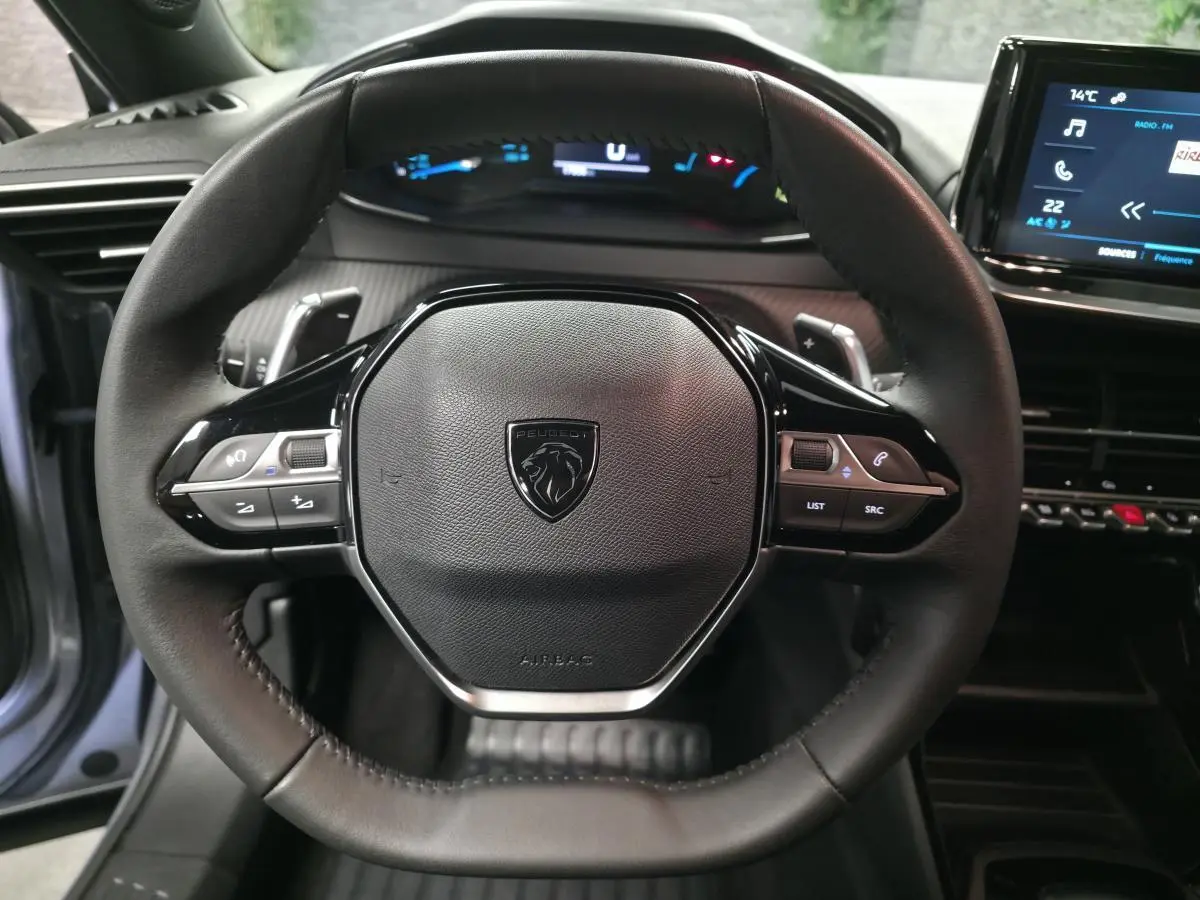 Vue rapprochée du volant compact cuir noir du Peugeot 2008 1.2i Hybrid 2025 avec commandes multimédia intégrées.