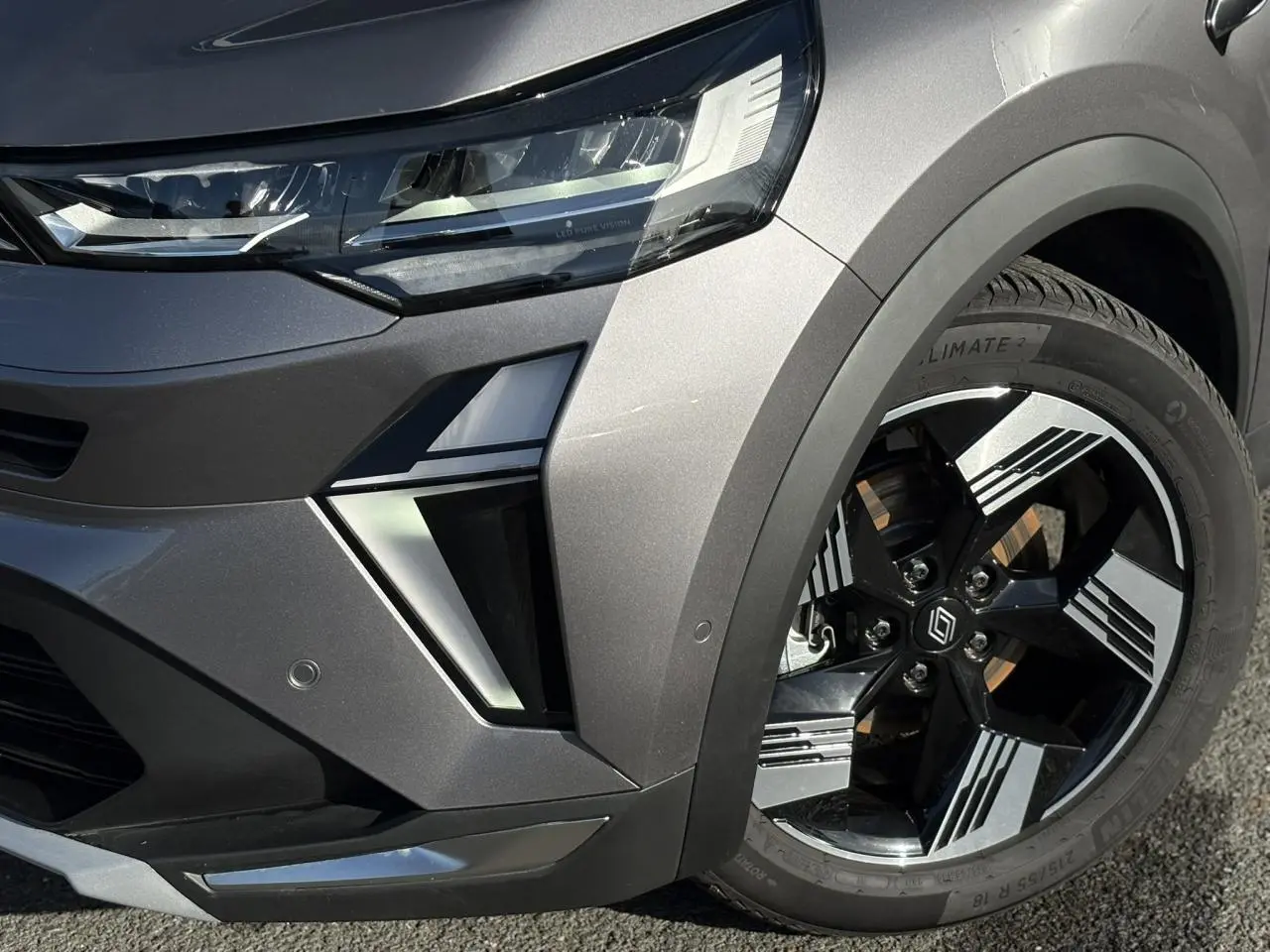 Gros plan sur l'avant droit gris Cassiopée du Renault SYMBIOZ E-Tech, mettant en valeur le phare LED et la jante 18 pouces.