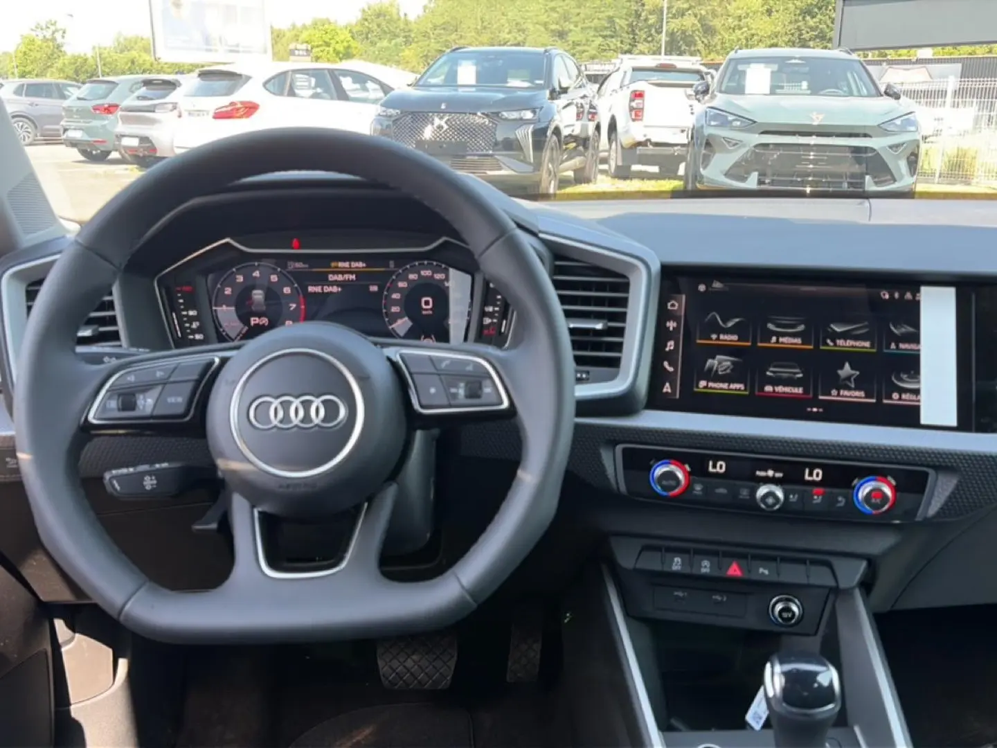 Vue intérieure centrée sur le volant Audi et le tableau de bord numérique avec écran tactile, ambiance moderne et épurée.
