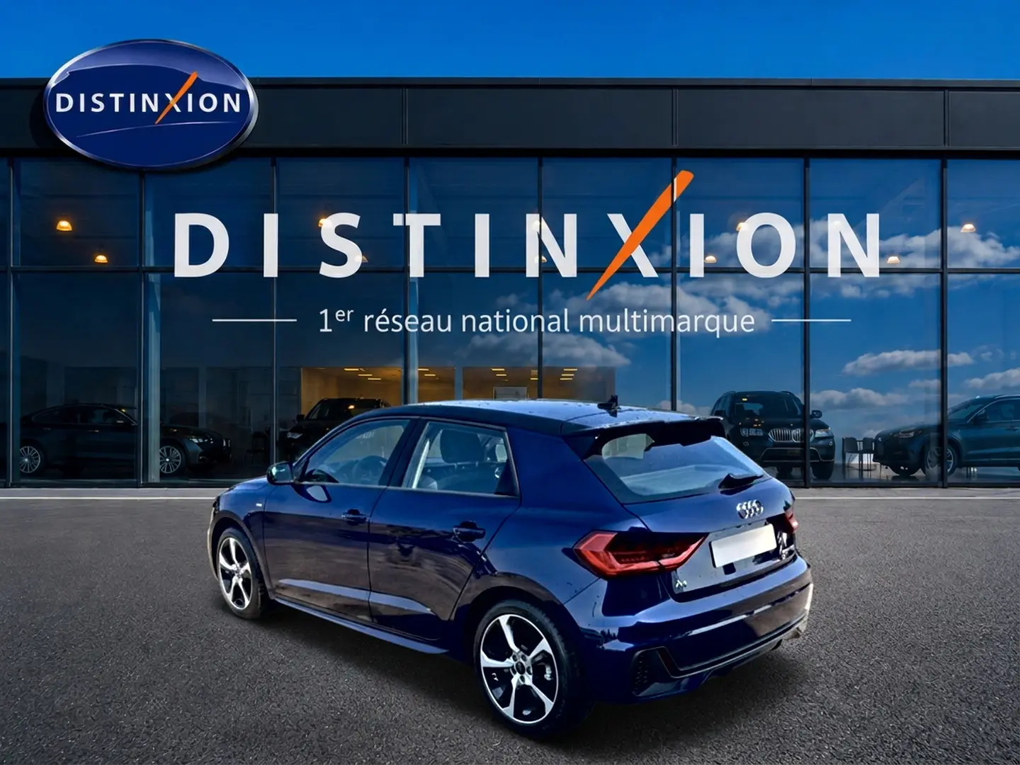 Audi A1 Sportback bleu foncé en 3/4 arrière droit, avec jantes alu et becquet arrière visible devant un showroom Distinxion.