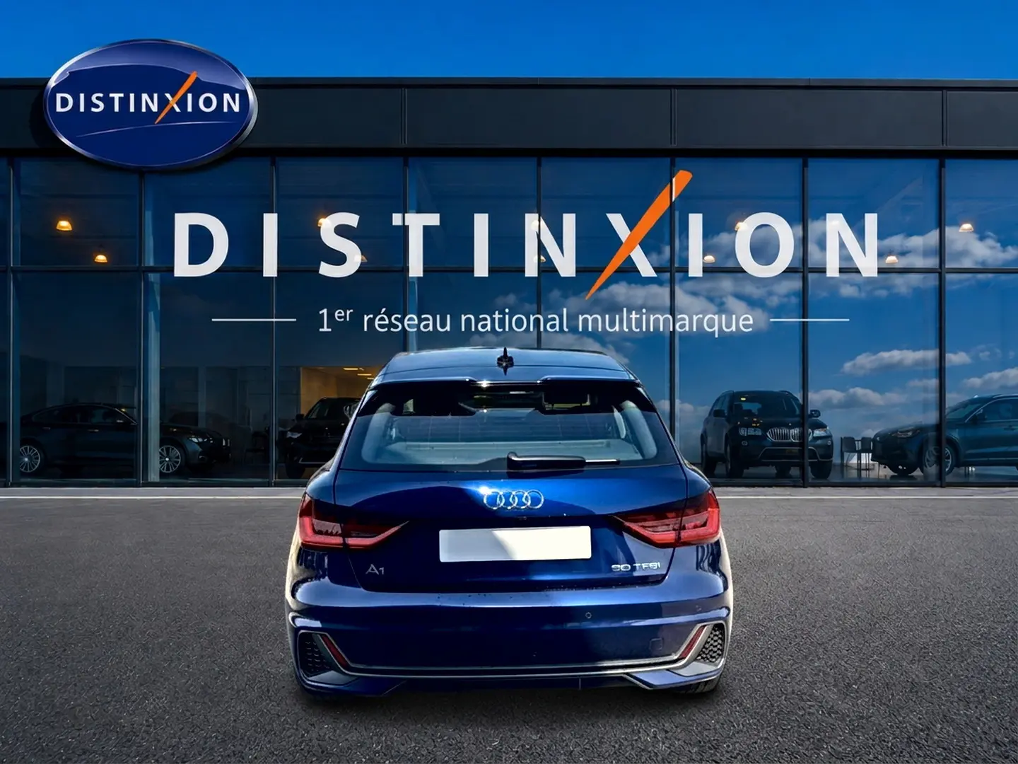 Vue arrière d'une Audi A1 Sportback 30 TFSI bleu foncé, avec feux LED et becquet arrière, devant une vitrine Distinxion.