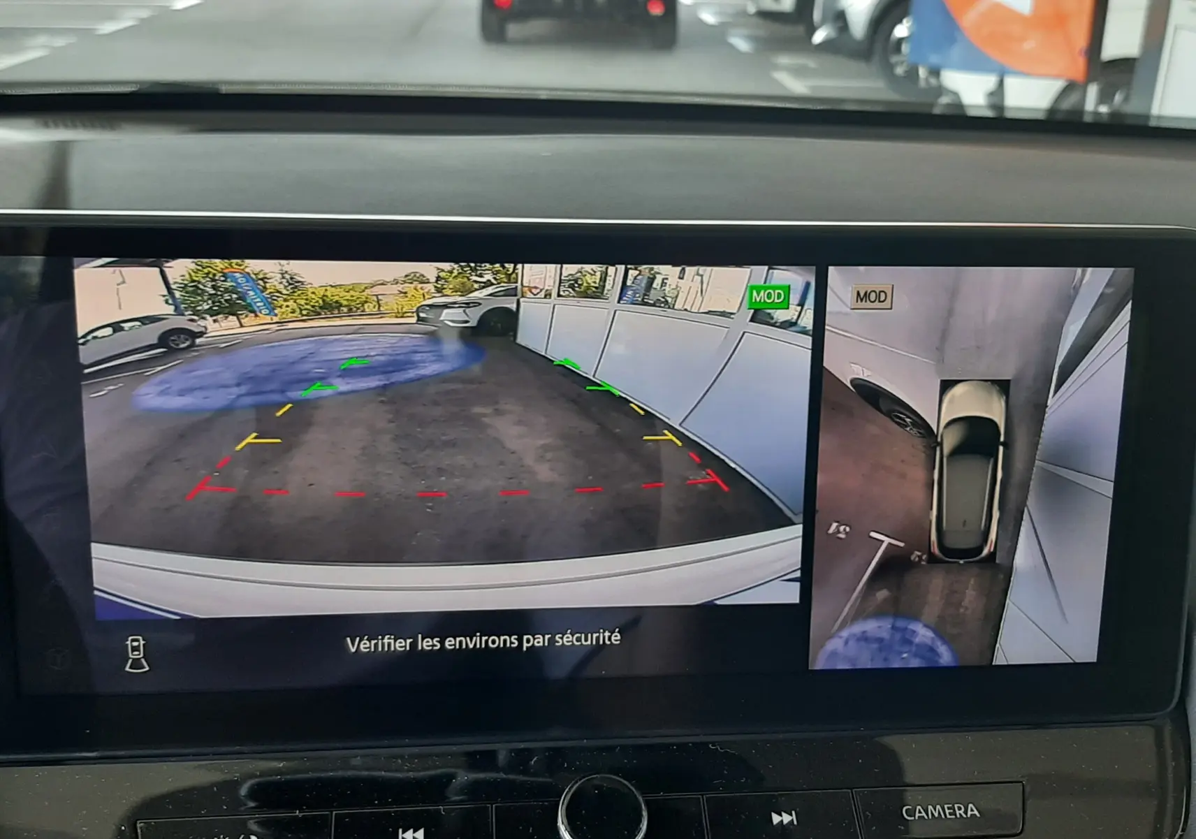 Écran de caméra 360° du Nissan Qashqai blanc lunaire montrant l'arrière et la vue aérienne du stationnement.