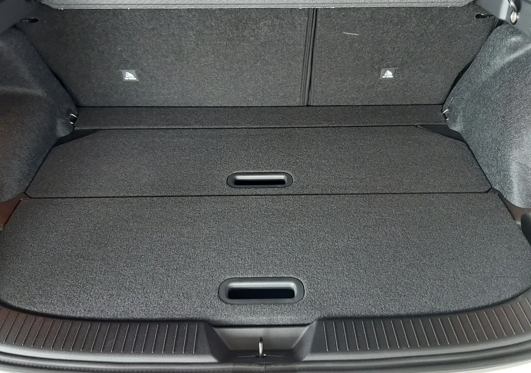 Coffre ouvert du Nissan Qashqai blanc lunaire 2022, montrant un espace de rangement plat et compartimenté en tissu gris foncé.