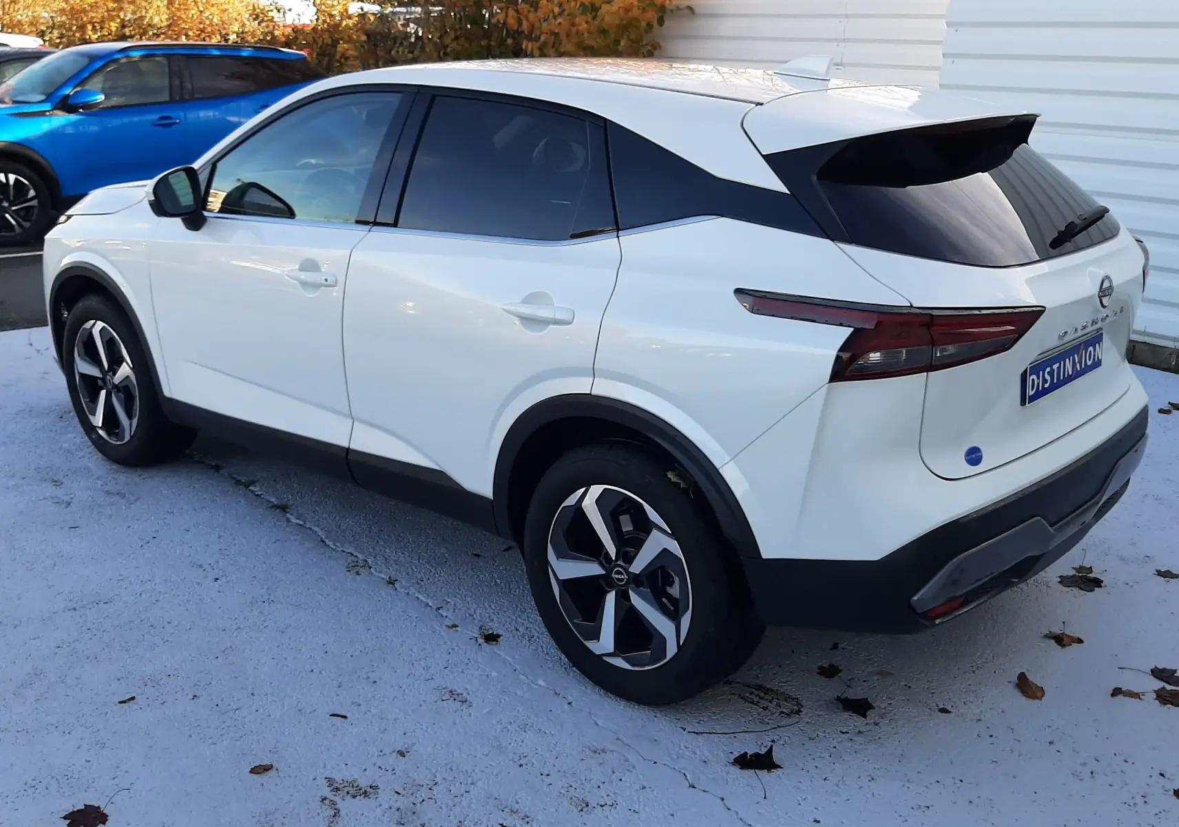 Nissan Qashqai blanc lunaire vu en 3/4 arrière droit, avec vitres teintées et jantes au design moderne.