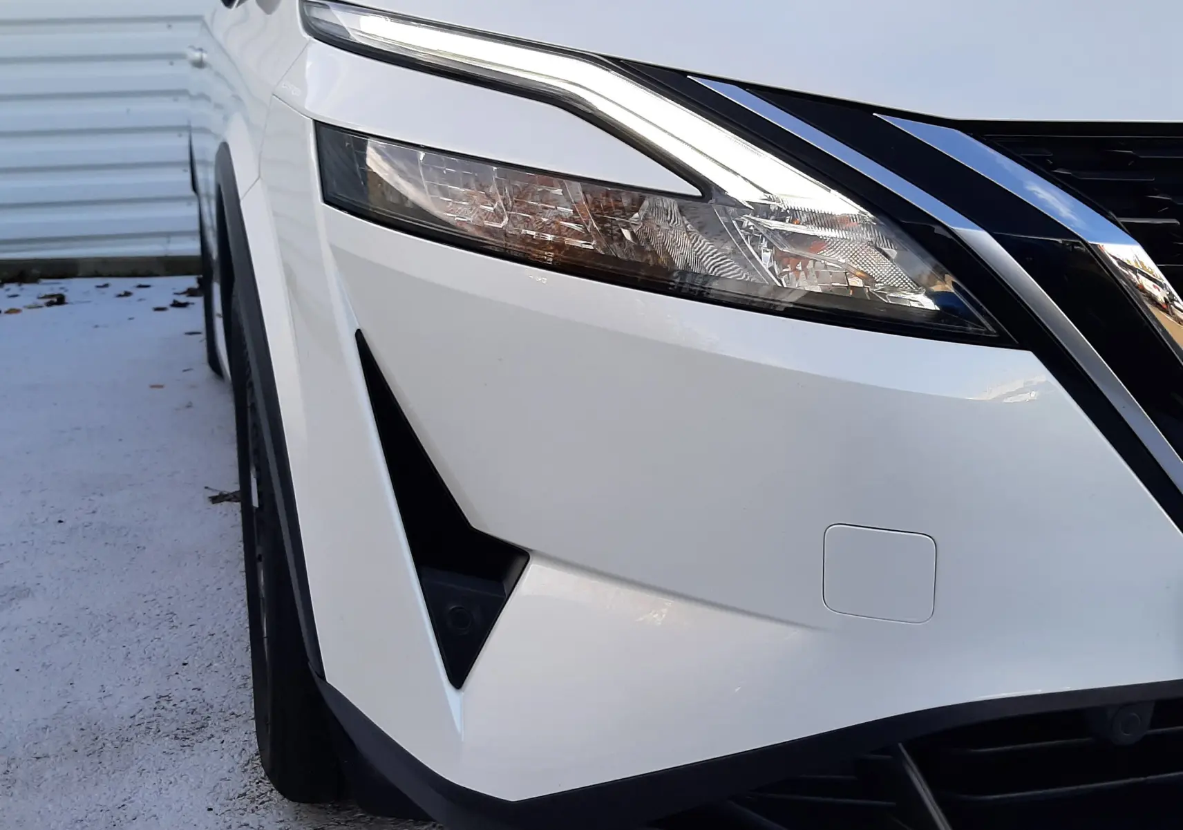 Gros plan sur l'avant gauche du Nissan Qashqai blanc lunaire 2022, mettant en valeur son phare LED et la calandre noire.