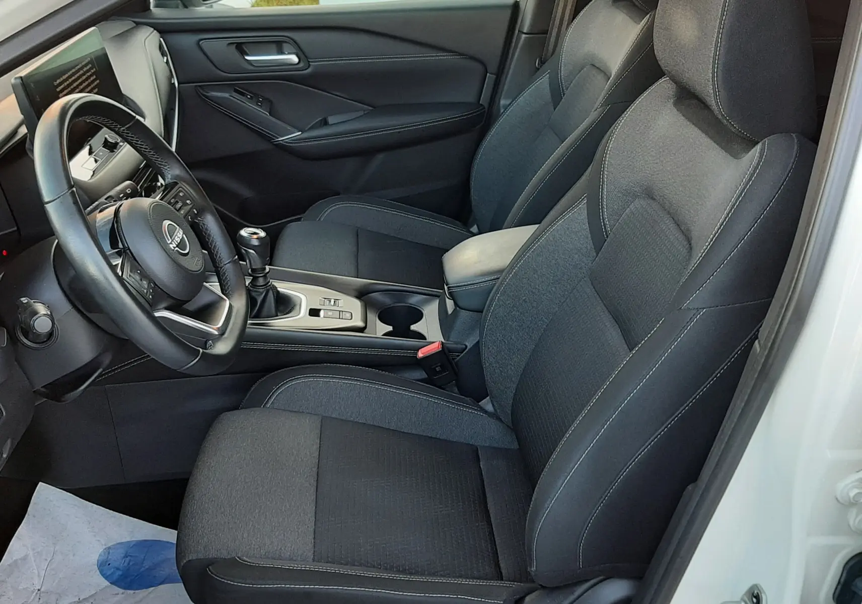 Vue intérieure côté conducteur du Nissan Qashqai blanc lunaire 2022, sièges tissu gris foncé et tableau de bord moderne.