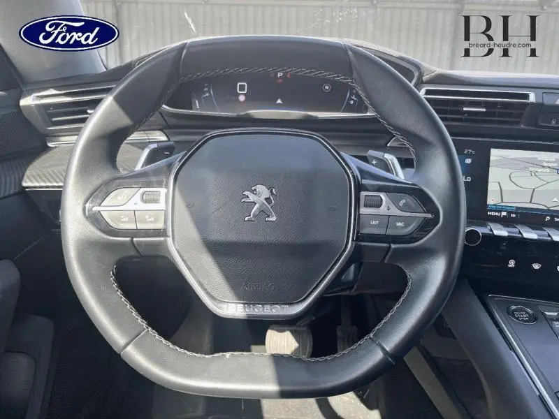 Vue rapprochée du volant cuir noir de la Peugeot 508 SW gris Artense, avec tableau de bord digital et écran tactile visible.