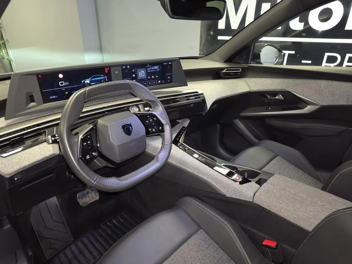 Intérieur avant droit du Peugeot 3008 Hybrid 2025, tableau de bord et volant cuir avec écrans numériques panoramiques.