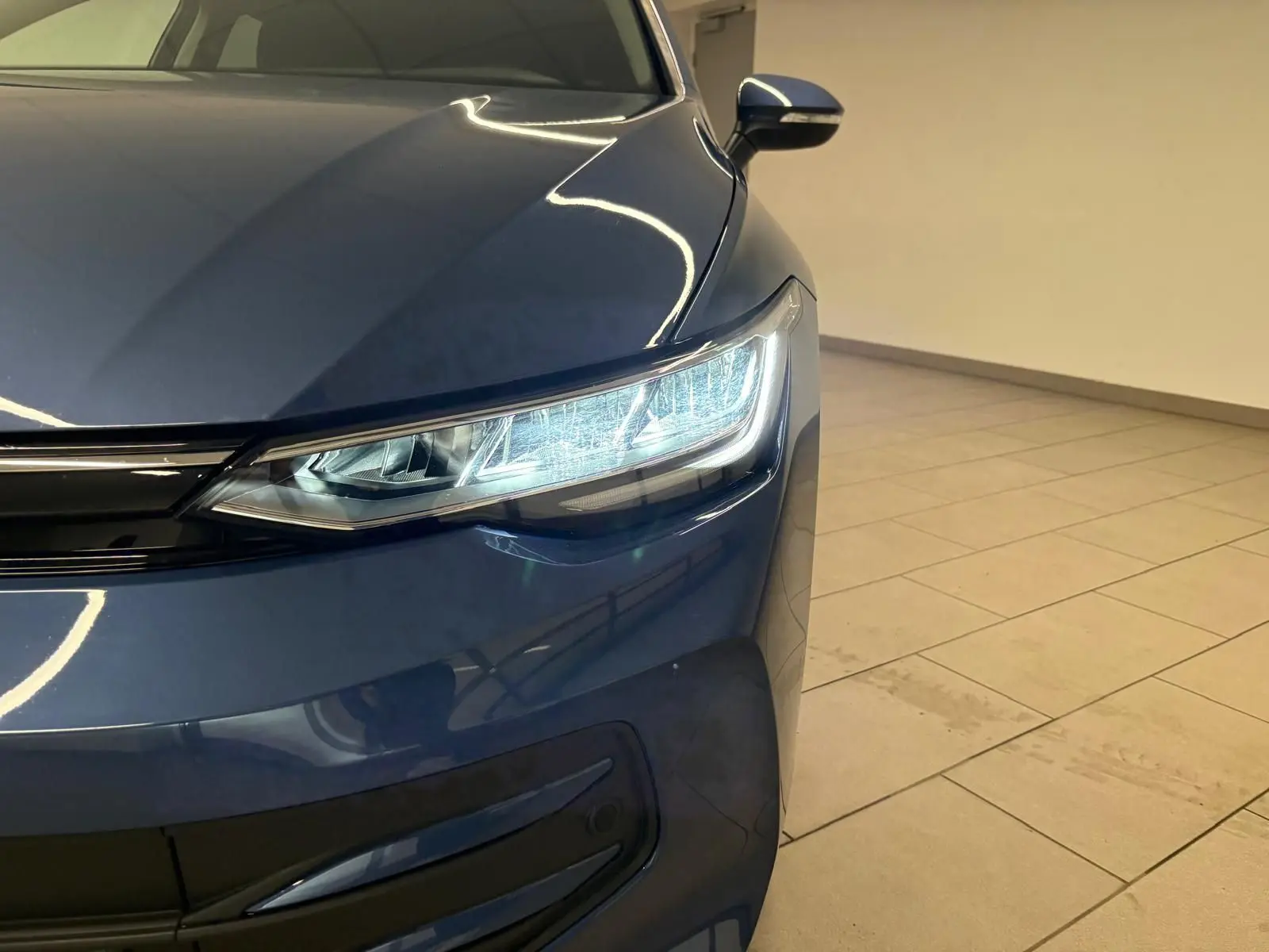 Gros plan sur l'avant droit d'une Volkswagen Golf 1.5 eTSI 2025 en Bleu Anémone avec phares LED allumés.