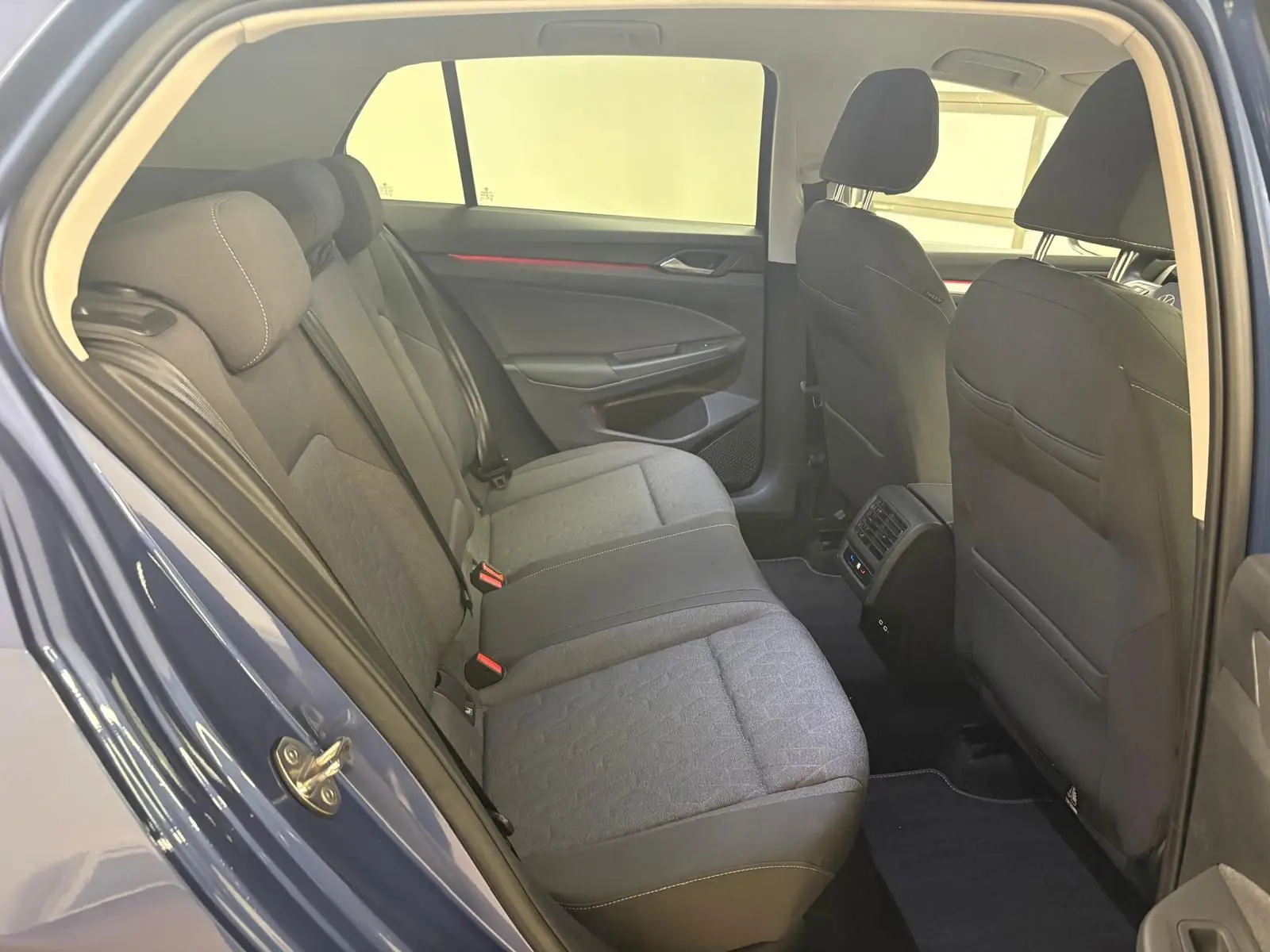 Vue intérieure arrière côté gauche de la Volkswagen Golf 1.5 eTSI 116 DSG7 Bleu Anémone, montrant les sièges arrière et les aérateurs centraux.