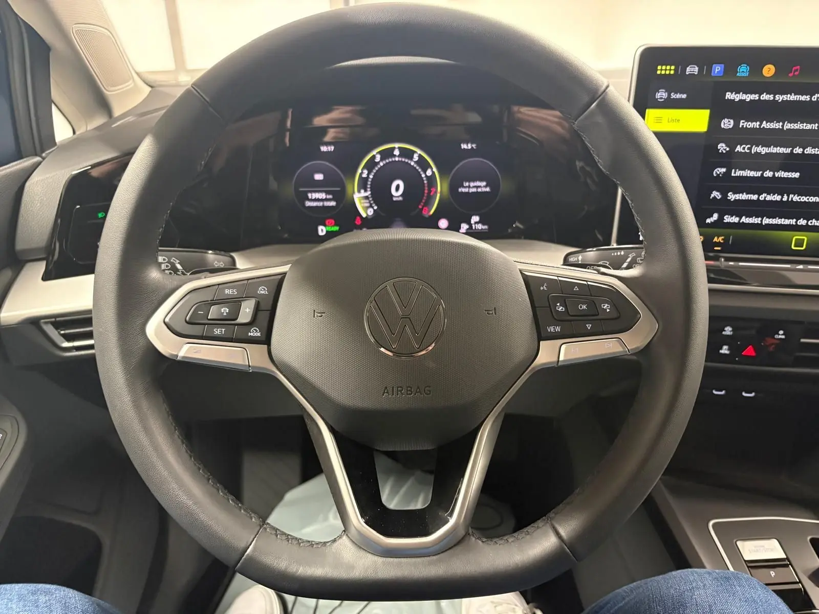 Vue rapprochée du volant multifonction noir de la Volkswagen Golf 1.5 eTSI 116 DSG7 avec tableau de bord numérique allumé.